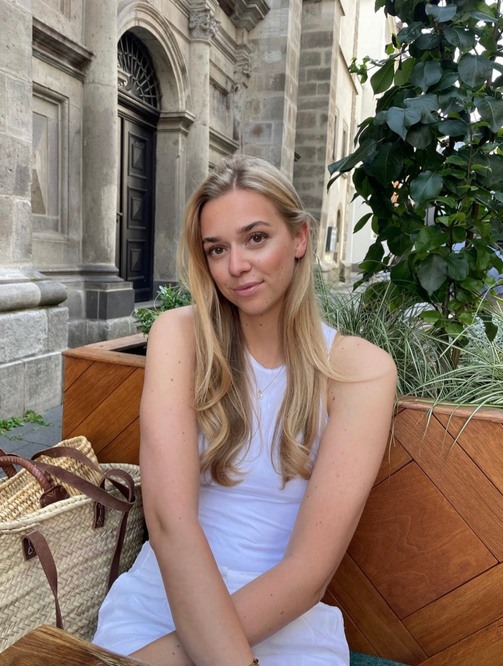 Woman in a white dress sitting outdoors with a stone building and plants in the background